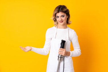 El blenderi kullanan kız sarı arkaplanda izole edilmiş bir şekilde bir reklam eklemek için kopyalama alanı tutuyor