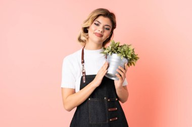 Rus bahçıvan kız pembe arka planda izole edilmiş bir bitki tutuyor alkışlıyor.