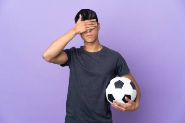 İzole edilmiş mor arka planı olan genç bir futbolcu gözlerini elleriyle kapatıyor. Bir şey görmek istemiyorum.