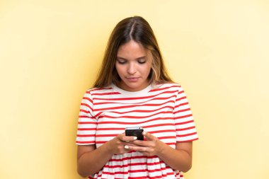 Sarı arka planda cep telefonu kullanan genç beyaz kadın.