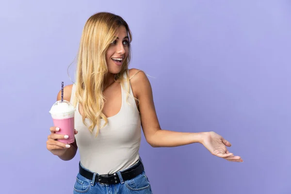 年轻的金发碧眼的乌拉圭女人 带着草莓奶昔 背景是紫色的 她面带微笑地看着旁边 — 图库照片