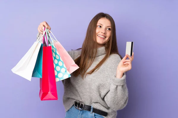 十几岁的高加索女孩被隔离在紫色背景下 手里拿着购物袋和信用卡 — 图库照片