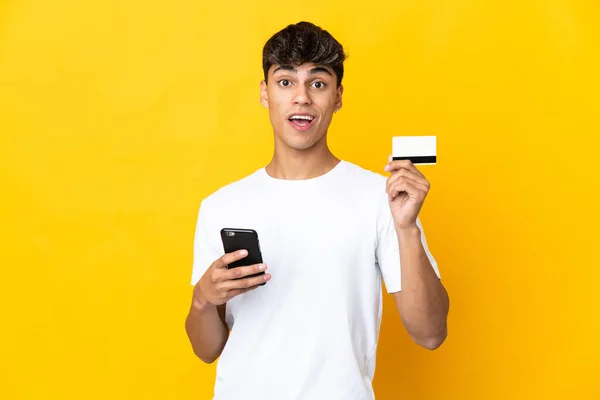 Mladý Muž Přes Izolované Žluté Pozadí Nákup Mobilem Držící Kreditní — Stock fotografie
