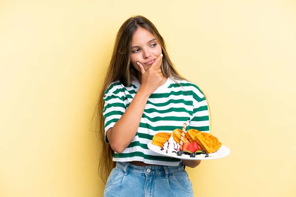 Jonge Kaukasische Vrouw Houden Wafels Geïsoleerd Gele Achtergrond Met Twijfels — Stockfoto