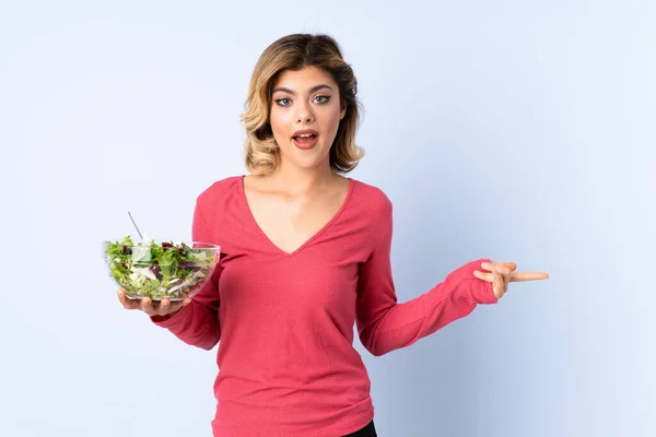 Mulher Adolescente Com Salada Isolada Fundo Azul Surpreendido Apontando Lado — Fotografia de Stock