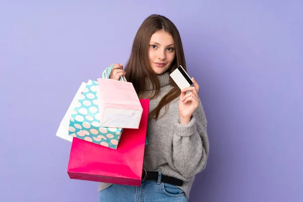 十几岁的高加索女孩被隔离在紫色背景下 手里拿着购物袋和信用卡 — 图库照片