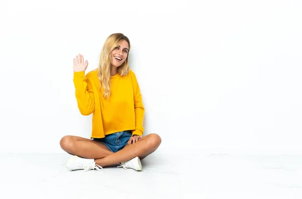 Jonge Blonde Uruguayaanse Vrouw Zit Vloer Geïsoleerd Witte Achtergrond Salueren — Stockfoto
