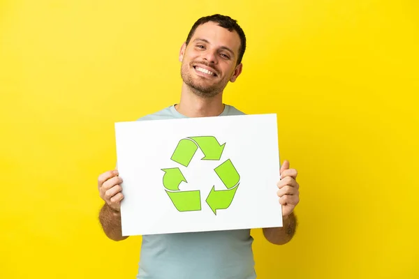 Brazylijczyk Nad Odizolowanym Fioletowym Tle Trzymając Tabliczkę Ikoną Recyklingu Szczęśliwym — Zdjęcie stockowe