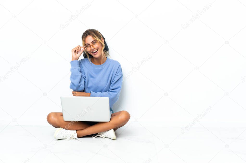 Young blonde Uruguayan girl with the laptop isolated on white background with glasses and happy