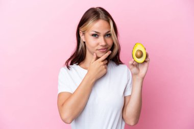 Avokado tutan genç Rus kadın pembe arka planda izole edilmiş.