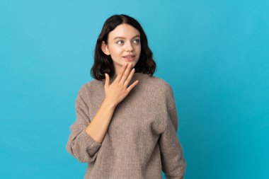 Genç Ukraynalı kız mavi arka planda izole edilmiş gülümserken yukarı bakıyor