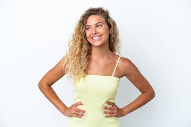 Beyaz arka planda izole edilmiş kıvırcık saçlı kolları kalçasında ve gülümseyen bir kız.