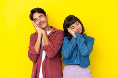 Sarı arka planda izole edilmiş genç melez bir çift, uyku jesti yapıyor.