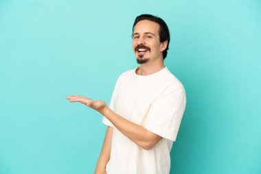 Mavi arka planda izole edilmiş genç beyaz adam gülümserken bir fikir sunuyor.