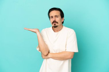 Kafkasyalı genç adam mavi arka planda izole edilmiş. Şüpheleri var.