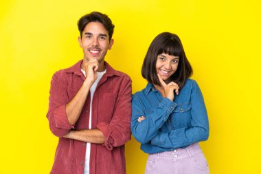 Sarı arka planda soyutlanmış, tatlı bir ifadeyle gülümseyen genç melez çift.
