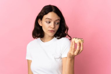 Genç Ukraynalı kız pembe arka planda izole edilmiş, elinde donut var.