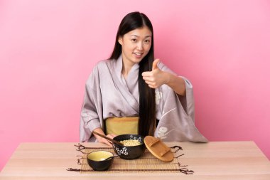 Genç Çinli kız kimono giyip başparmaklarıyla erişte yiyor çünkü iyi bir şey oldu.