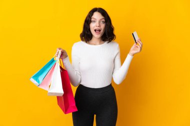 Sarı arka planda izole edilmiş genç Ukraynalı kız elinde alışveriş torbalarıyla şaşırmış.