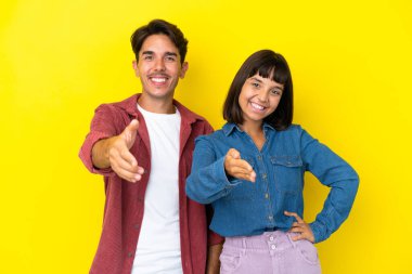 Genç melez çift sarı arka planda izole edilmiş iyi bir anlaşma için el sıkışıyorlar.