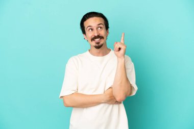 Mavi arka planda izole edilmiş genç beyaz adam harika bir fikre işaret ediyor.