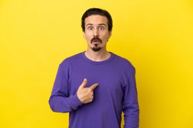Sarı arka planda izole edilmiş genç beyaz adam kendini işaret ediyor.