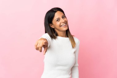 Pembe arka planda izole edilmiş beyaz kız mutlu bir ifadeyle ön tarafı işaret ediyor.