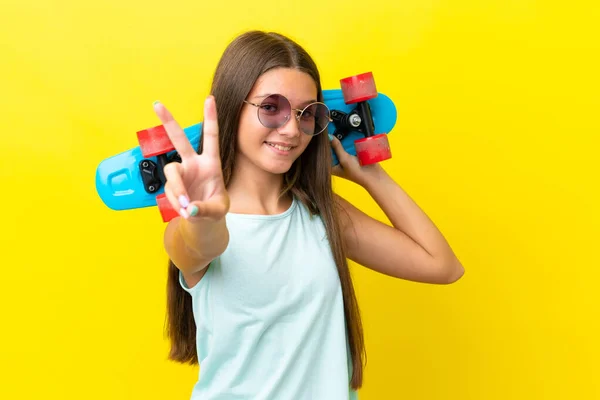 小さなCaucasian Skatter女の子絶縁上の黄色の背景とともにスケート行います勝利ジェスチャー — ストック写真