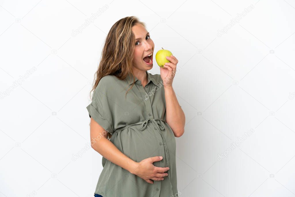 Young caucasian woman isolated on white background pregnant and holding an apple and eating it