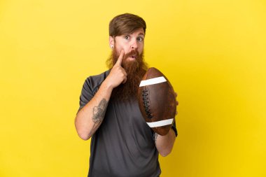 Kızıl saçlı beyaz adam sarı arka planda ragbi oynuyor. 