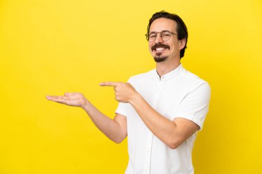 Sarı arka planda izole edilmiş genç beyaz bir adam bir ilan vermek için avucunun içinde hayali bir fotokopi makinesi tutuyor.