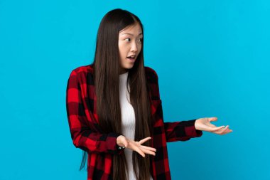 Genç Çinli bir kız mavi arka planda, sürpriz bir ifadeyle yan yana bakarken.