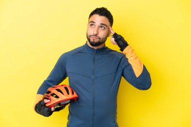 Genç bisikletçi Arap, sarı arka planda izole edilmiş. Şüpheleri ve düşünceleri var.