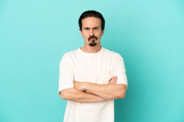 Mavi arka planda izole edilmiş genç beyaz bir adam üzgün hissediyor.