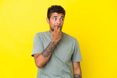 Genç yakışıklı Brezilyalı adam sarı arka planda izole edilmiş gergin ve korkmuş.