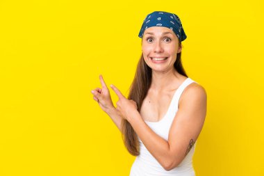 Sarı arka planda izole edilmiş genç bir İngiliz kadın korkmuş ve kenarı işaret ediyor.