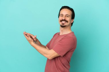 Mavi arka planda izole edilmiş genç beyaz adam alkışlıyor.