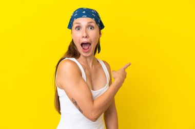Sarı arka planda izole edilmiş genç bir İngiliz kadın şaşırmış ve işaret ediyor.