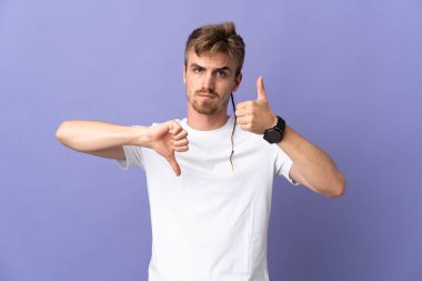 Mor arka planda izole edilmiş yakışıklı sarışın adam iyiye-kötüye işaret yapıyor. Evet ya da hayır arasında kararsız