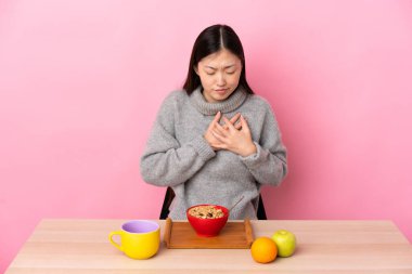 Genç Çinli bir kız masada kahvaltı yapıyor. Yüreği sızlıyor.