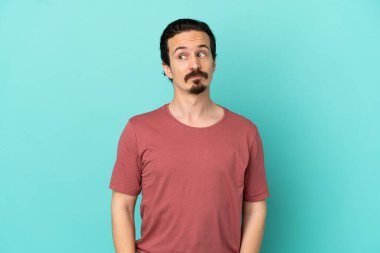 Mavi arka planda izole edilmiş genç beyaz adam şüpheli hareketler yapıyor.