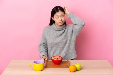 Genç Çinli bir kız kahvaltı yapıyor. Kafası kaşınırken şüpheyle karışık.