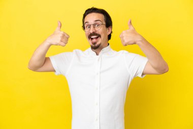 Sarı arka planda izole edilmiş genç beyaz bir adam baş parmak hareketi yapıyor.