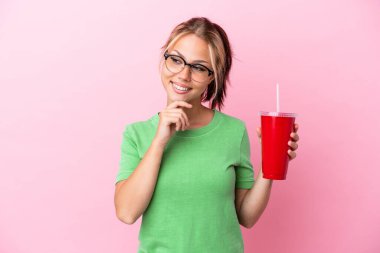 Genç Rus kadın pembe arka planda izole edilmiş bir ferahlatıcı tutuyor yan bakıyor ve gülümsüyor.