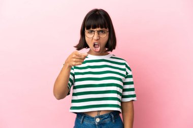 Pembe arka planda izole edilmiş genç melez kadın hayal kırıklığına uğramış ve ön tarafı işaret ediyor.