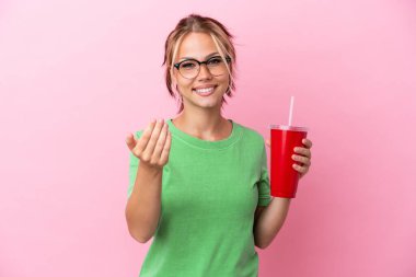 Genç Rus kadın pembe arka planda izole edilmiş bir ferahlatıcı tutuyor. Bizimle gelmesi için davet ediyor. Gelmene sevindim.