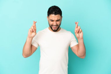 Genç Arap adam mavi arka planda izole edilmiş ve şans diliyor.