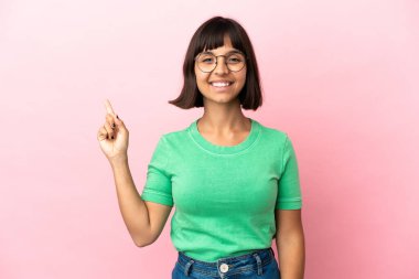 Pembe arka planda soyutlanmış genç melez kadın mutlu ve dik duruyor.