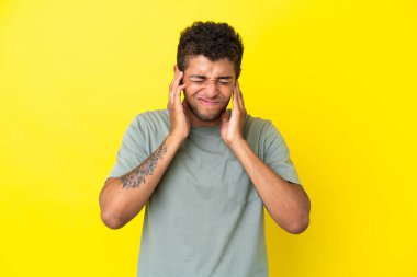 Sarı arka planda izole edilmiş yakışıklı Brezilyalı adam hayal kırıklığına uğramış ve kulaklarını kapatmış.