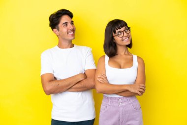 Sarı arka planda soyutlanmış genç melez çift gülümserken yukarı bakıyor.